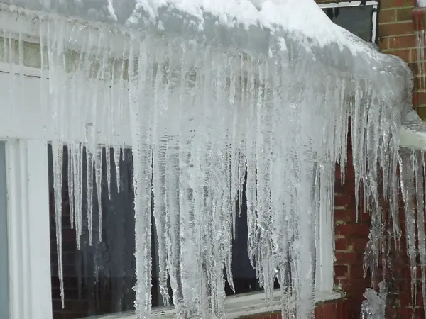 Large icicles hanging from a roof edge over a brick wall