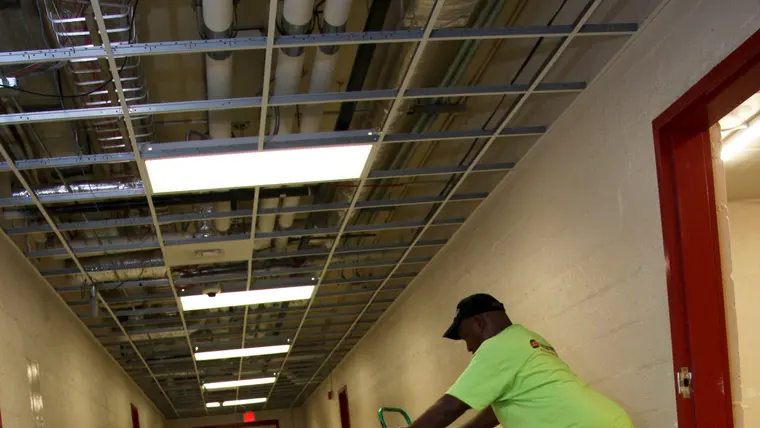 Worker stripping water-damaged floor tiles in a hallway with drying equipment