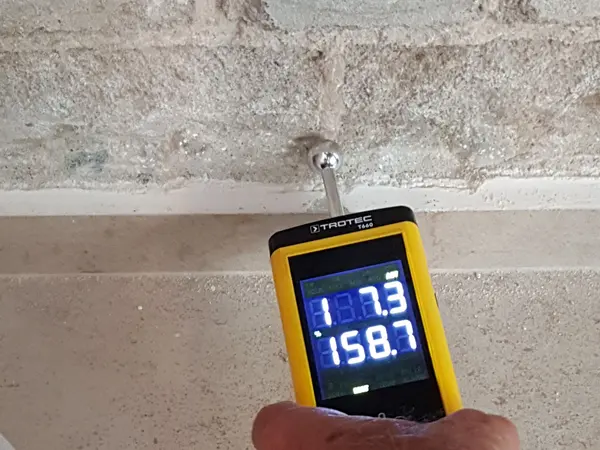 Hand holding a moisture meter against a surface