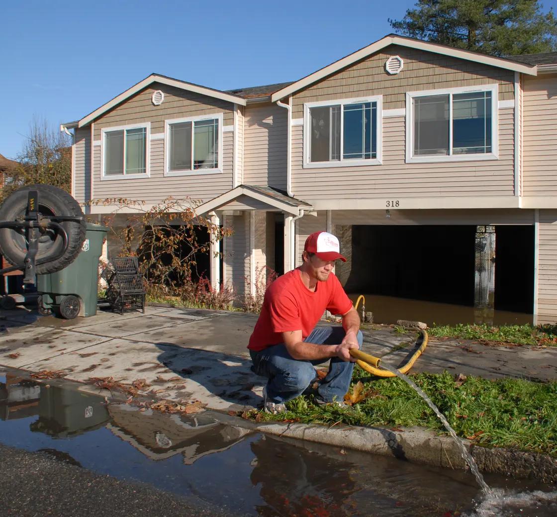 Man pumping water out of a flooded house through a hose