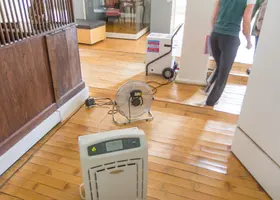 Volunteer carrying a fan and a dehumidifier into a brick house