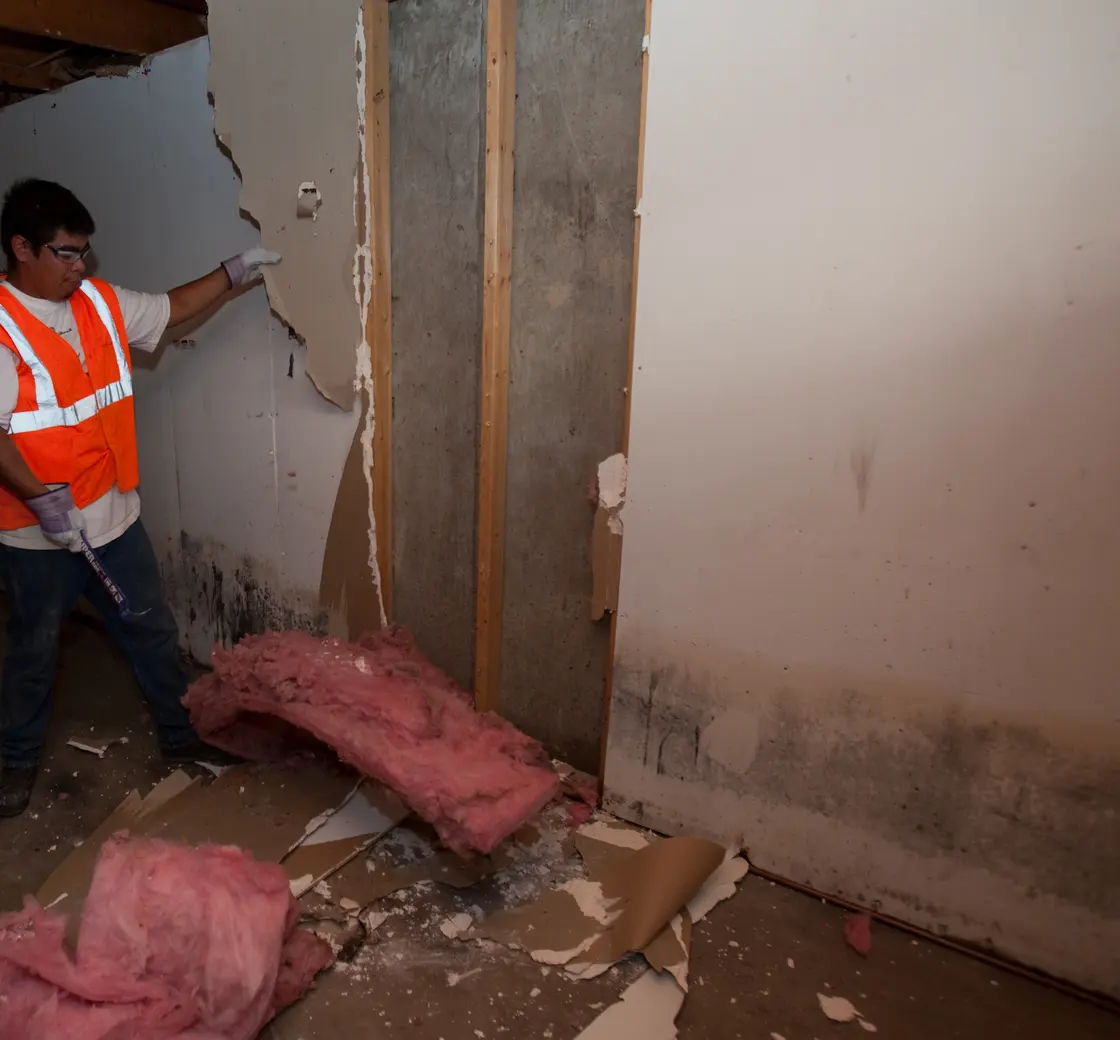 Worker cutting out wet drywall in a water-damaged basement